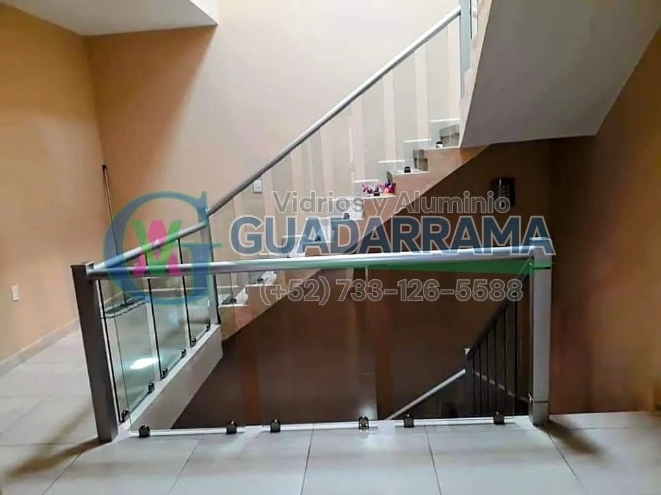 Barandal de vidrio templado con perfilería de aluminio blanco, instalado en escalera interior para dar seguridad sin perder la sensación de amplitud.