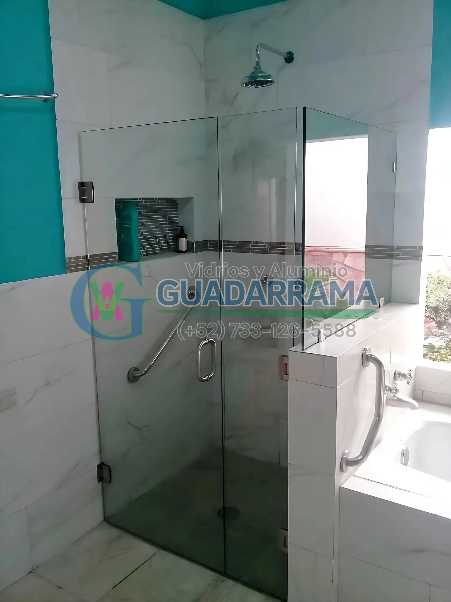 Cancel de baño en vidrio templado transparente con herraje abatible y agarradera de acero, instalado sobre muros forrados en mármol.