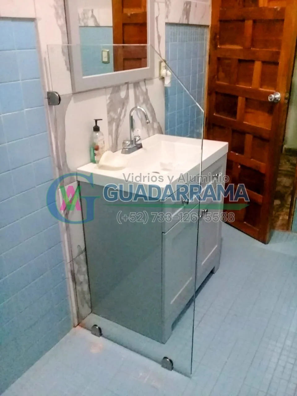 Cancel de baño en vidrio templado transparente, instalado como fijo divisor junto al mueble de lavabo.