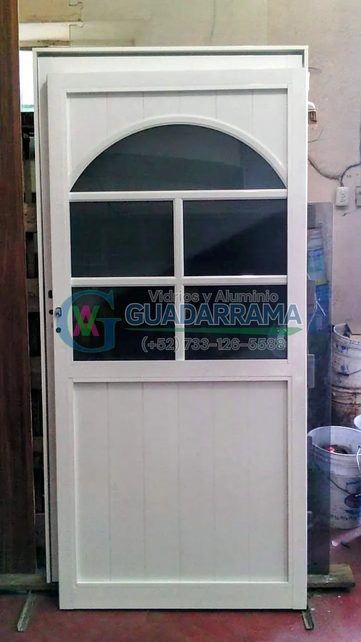 Puerta abatible en aluminio blanco con diseño de arco superior, vidrio tintex para privacidad y panel inferior con duela lisa.