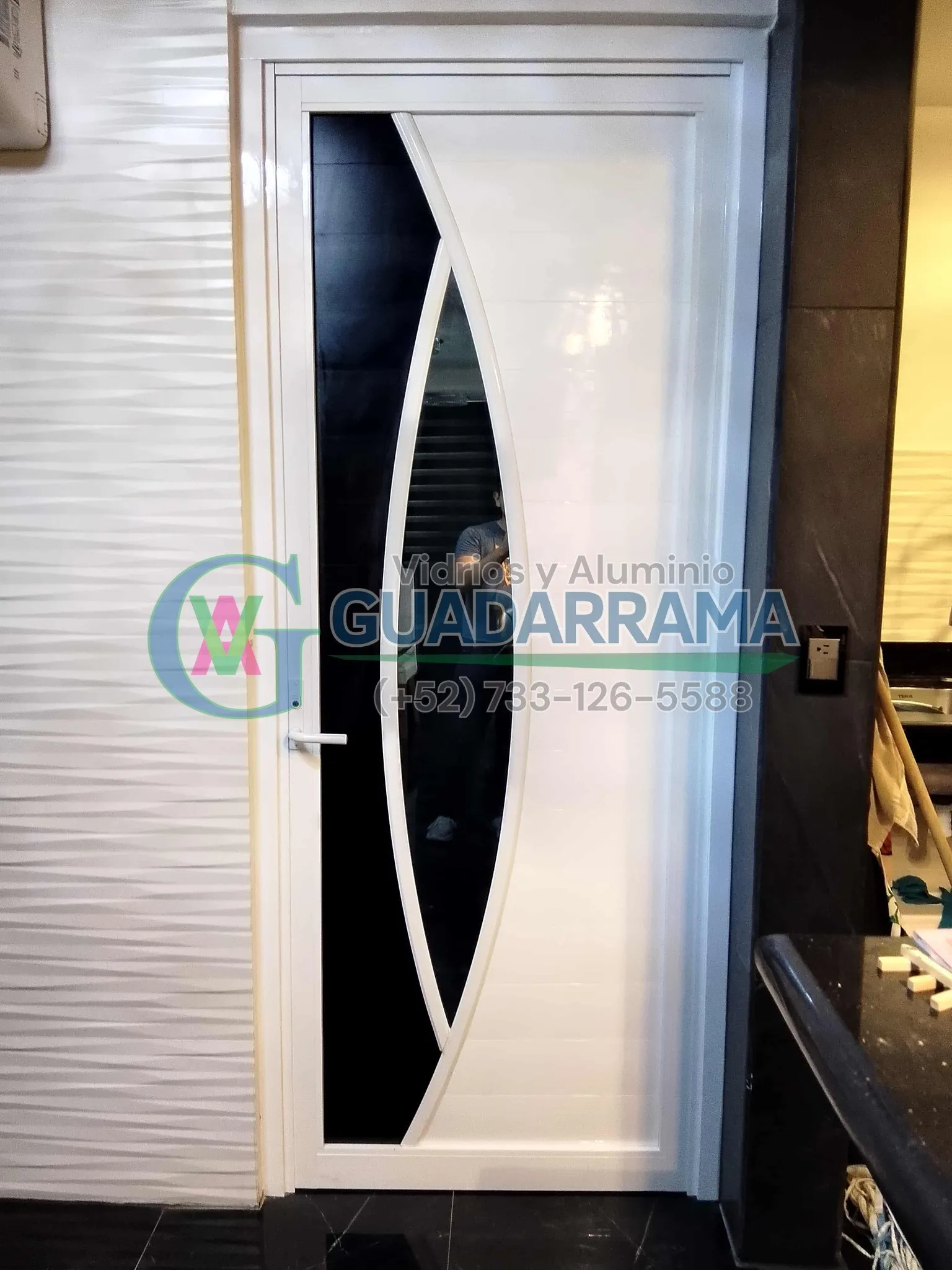 Puerta abatible en aluminio blanco con panel de vidrio curvo color filtrasol, acabada con duela lisa para un cierre limpio y de gran resistencia.
