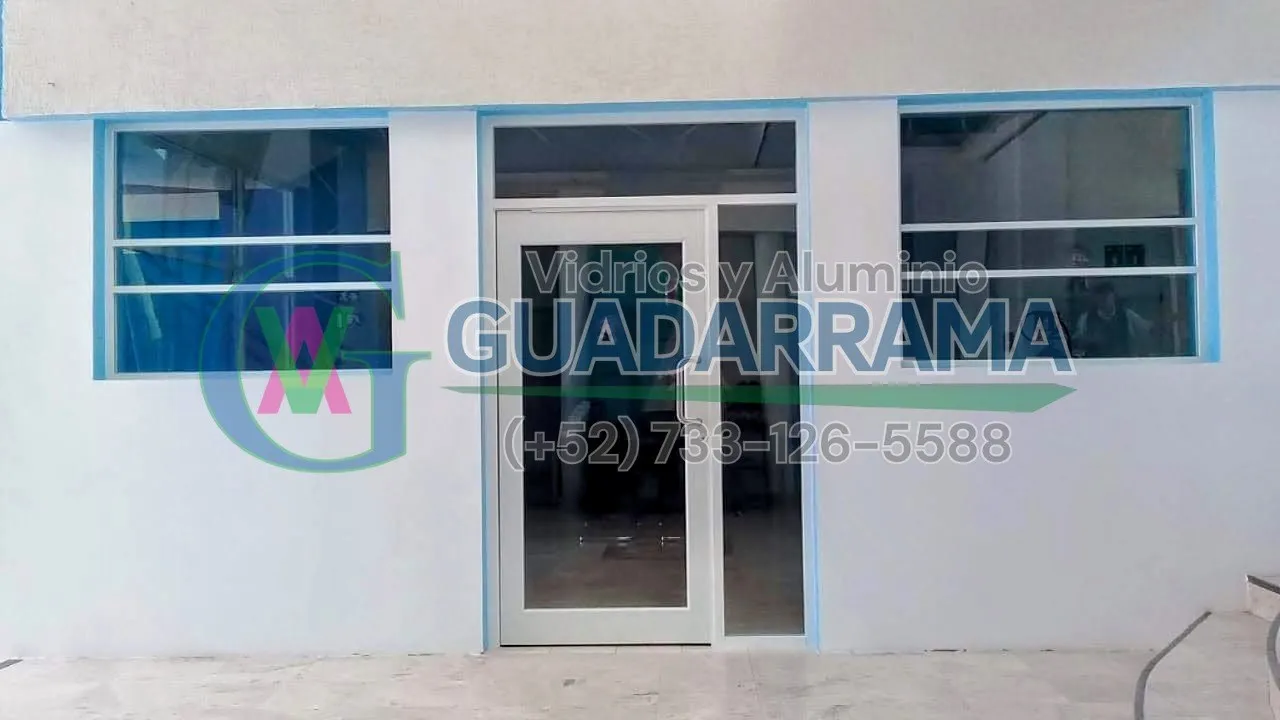 Instalamos esta puerta abatible de aluminio en blanco con vidrio transparente para una oficina, acompañada de dos paños fijos laterales que mantienen el espacio luminoso y con flui
