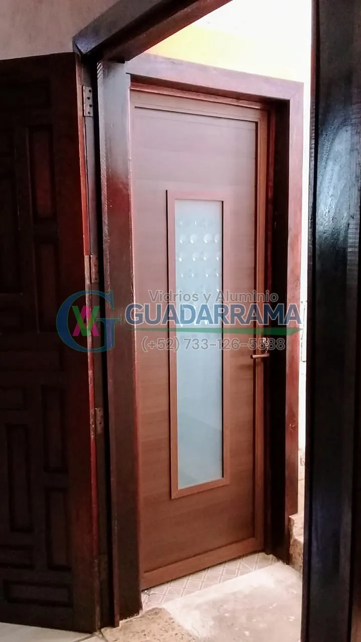 Puerta abatible en  aluminio acabado madera con detalle central de vidrio esmerilado: un toque de privacidad sin renunciar a la luz.
