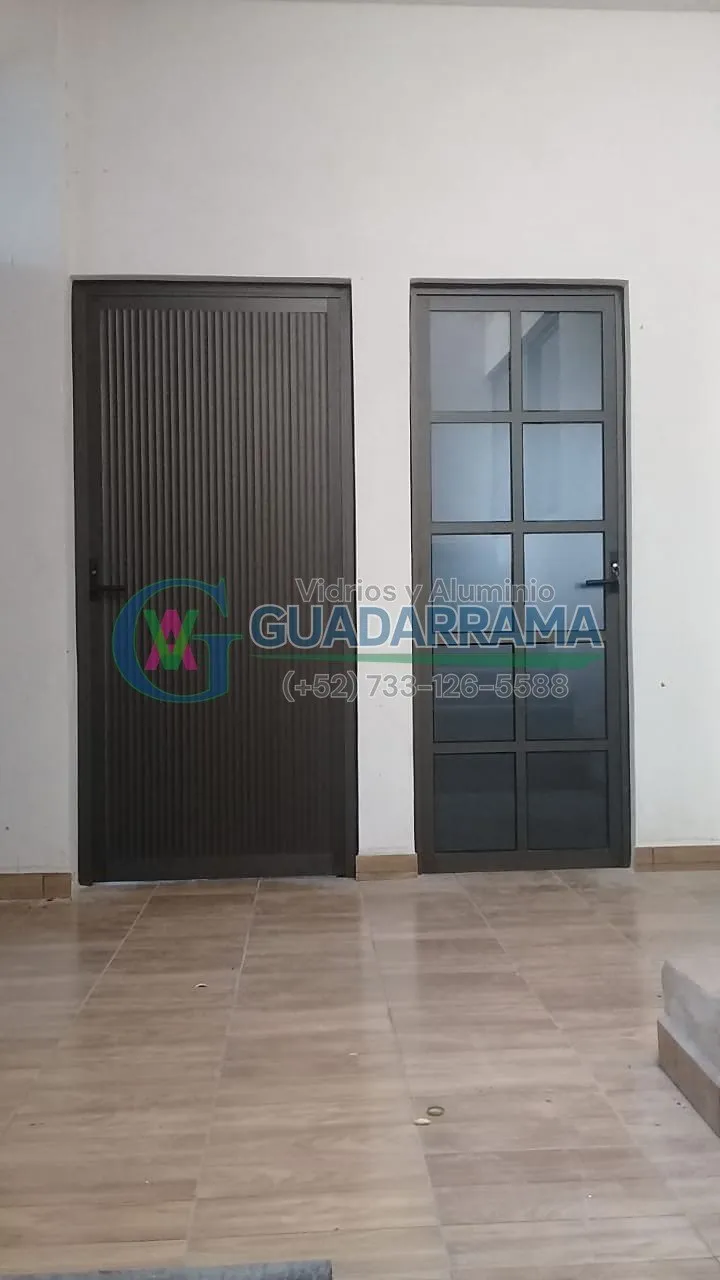 Puerta abatible en aluminio negro con panel de vidrio filtrasol, ideal para controlar la luz solar directa sin sacrificar la iluminación.
