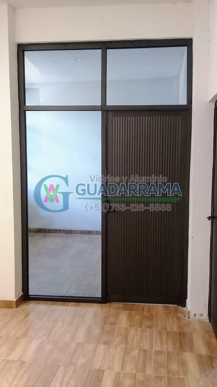 La duela de ondas le da un toque de diseño especial a esta puerta abatible en aluminio color negro con vidrio transparente.