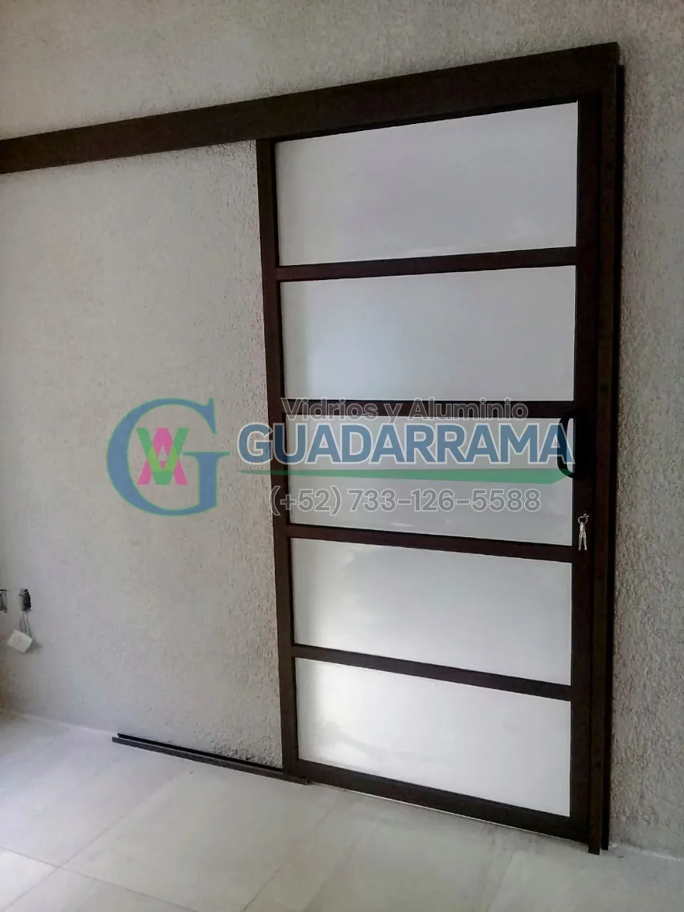 Puerta corrediza de aluminio en acabado nogal con vidrio esmerilado de 6 mm, ideal para separar ambientes en oficina con privacidad sin perder luz natural.