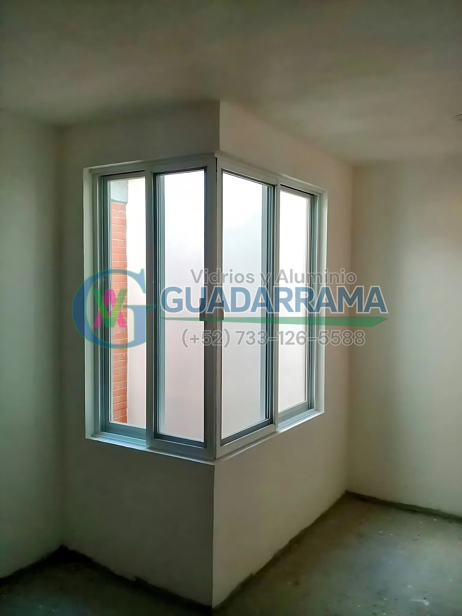 Ventana de esquina con cancel corredizo de aluminio blanco y vidrio esmerilado, instalada en un espacio en obra gris.